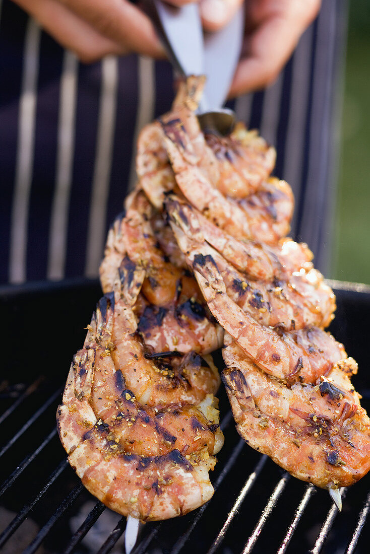 Taking prawn skewers off a barbecue