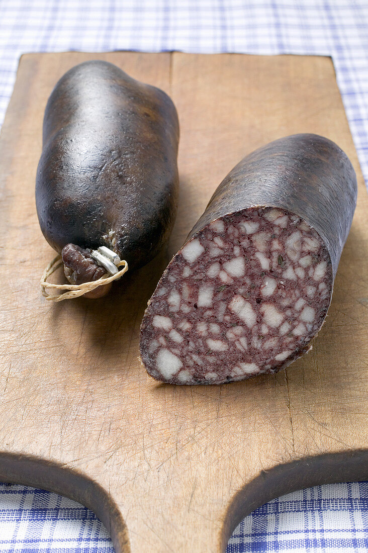 Two black puddings on chopping board, one with a piece removed