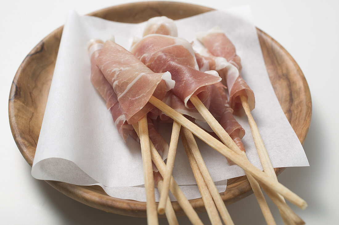 Grissini wrapped in raw ham on wooden plate