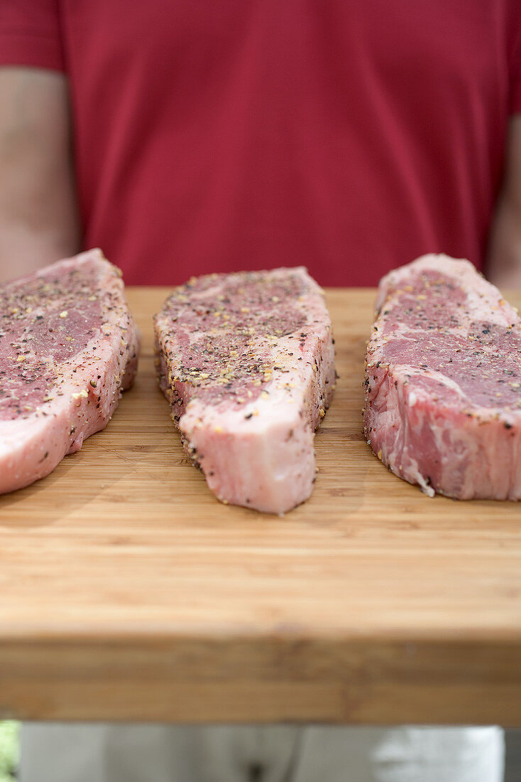 Seasoned steaks on chopping board, man in background