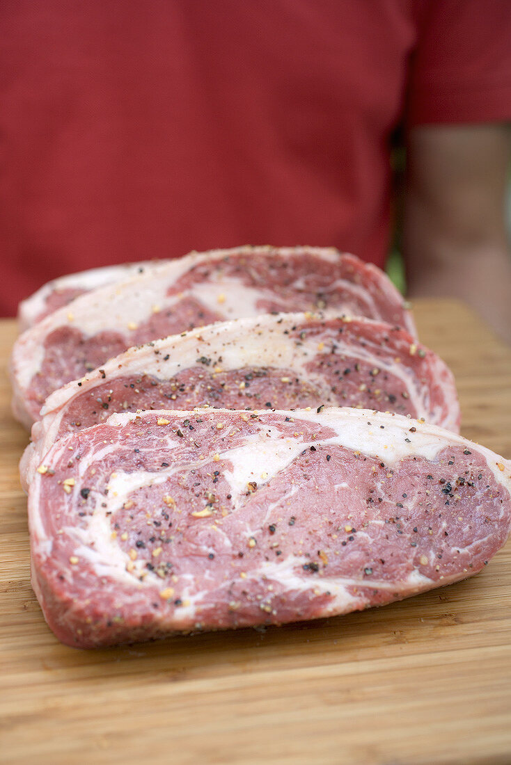 Seasoned steaks on chopping board, man in background