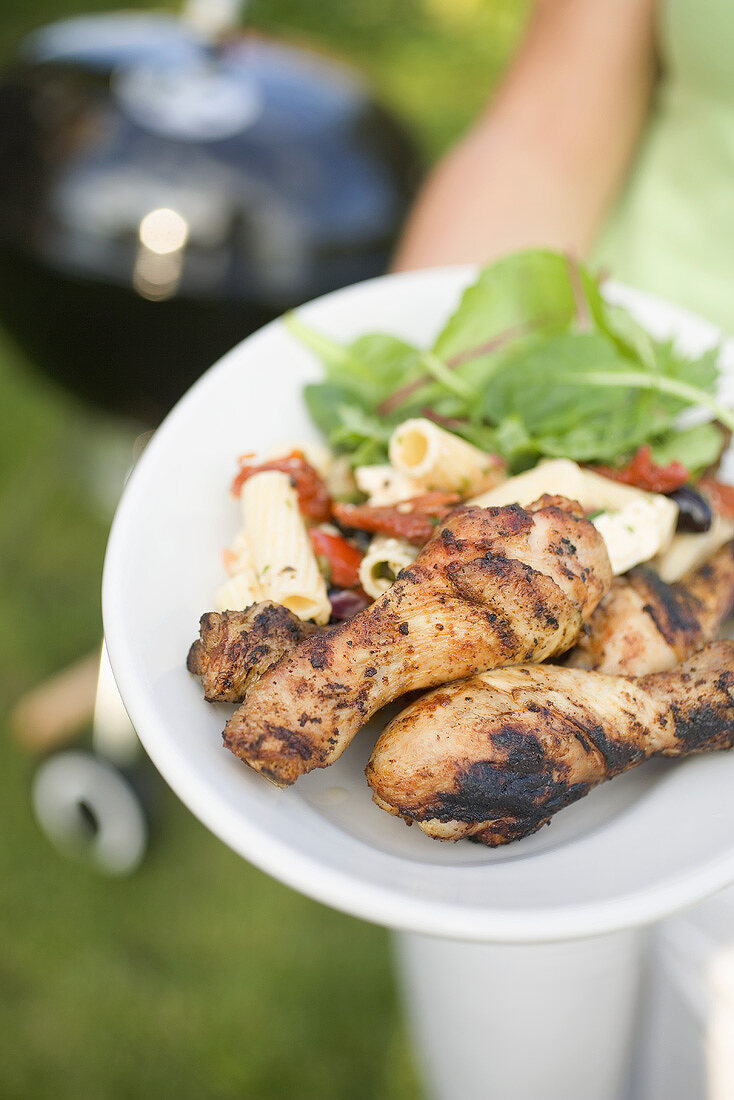 Woman holding plate of grilled chicken legs & pasta salad