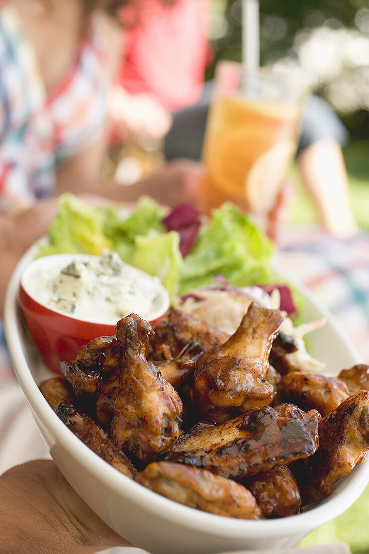 Hände halten Chicken Wings mit Salat, Menschen im Hintergrund