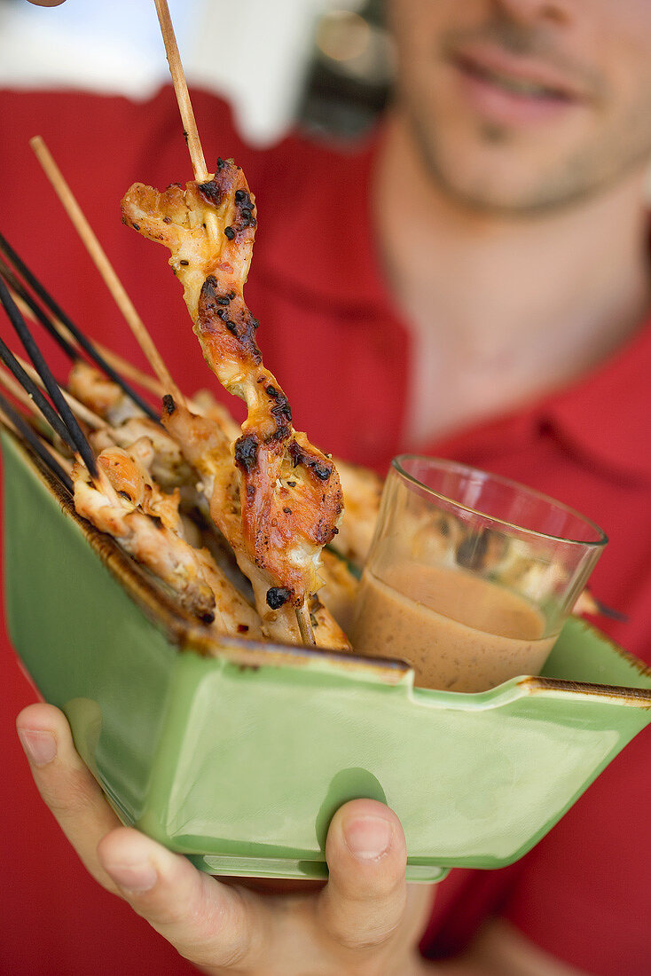 Man serving grilled satay with dip