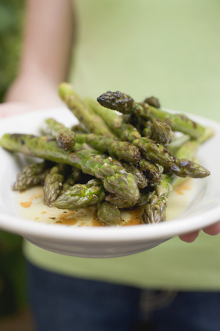Person holding a plate of grilled green asparagus