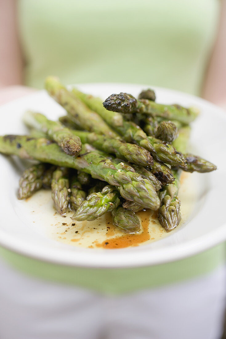 Woman holding a plate of grilled green asparagus