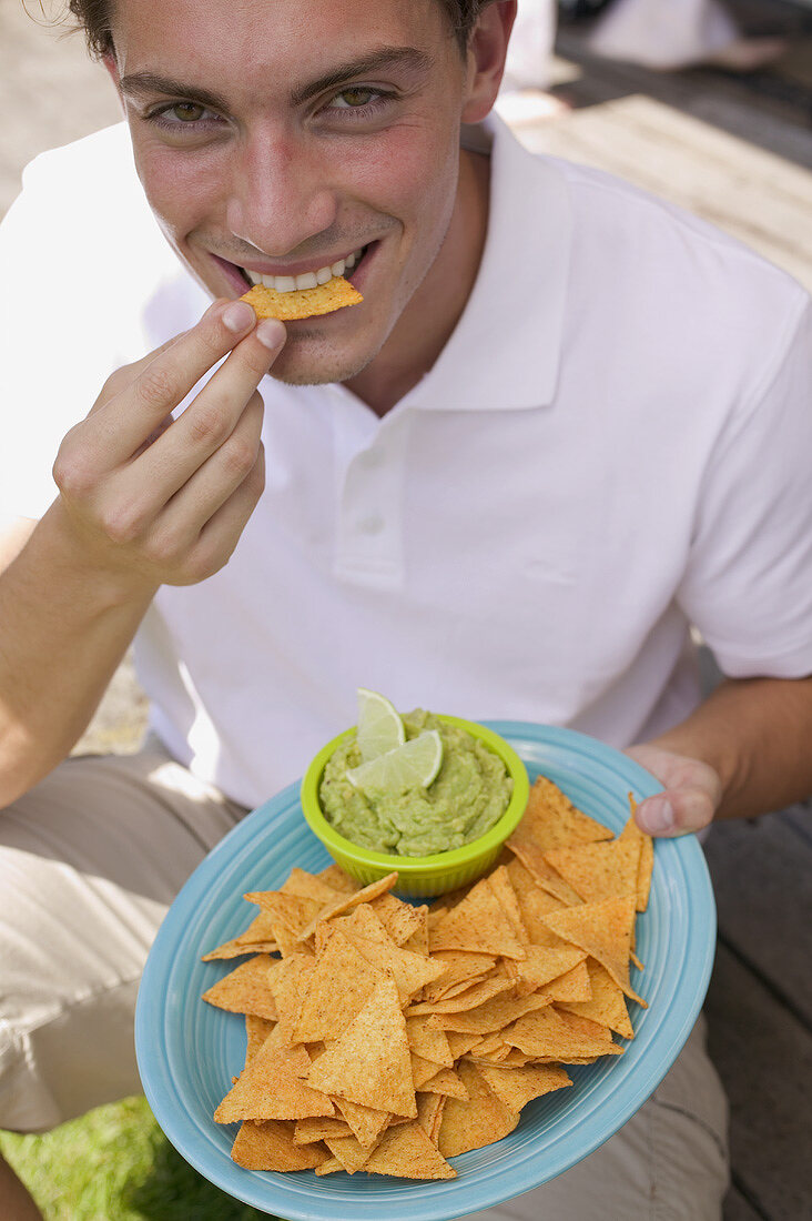 Young man eating tortilla chips with guacamole