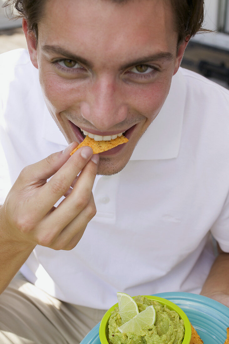 Young man eating tortilla chips with guacamole