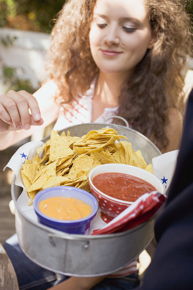 Woman reaching for tortilla chips with two dips in bowl