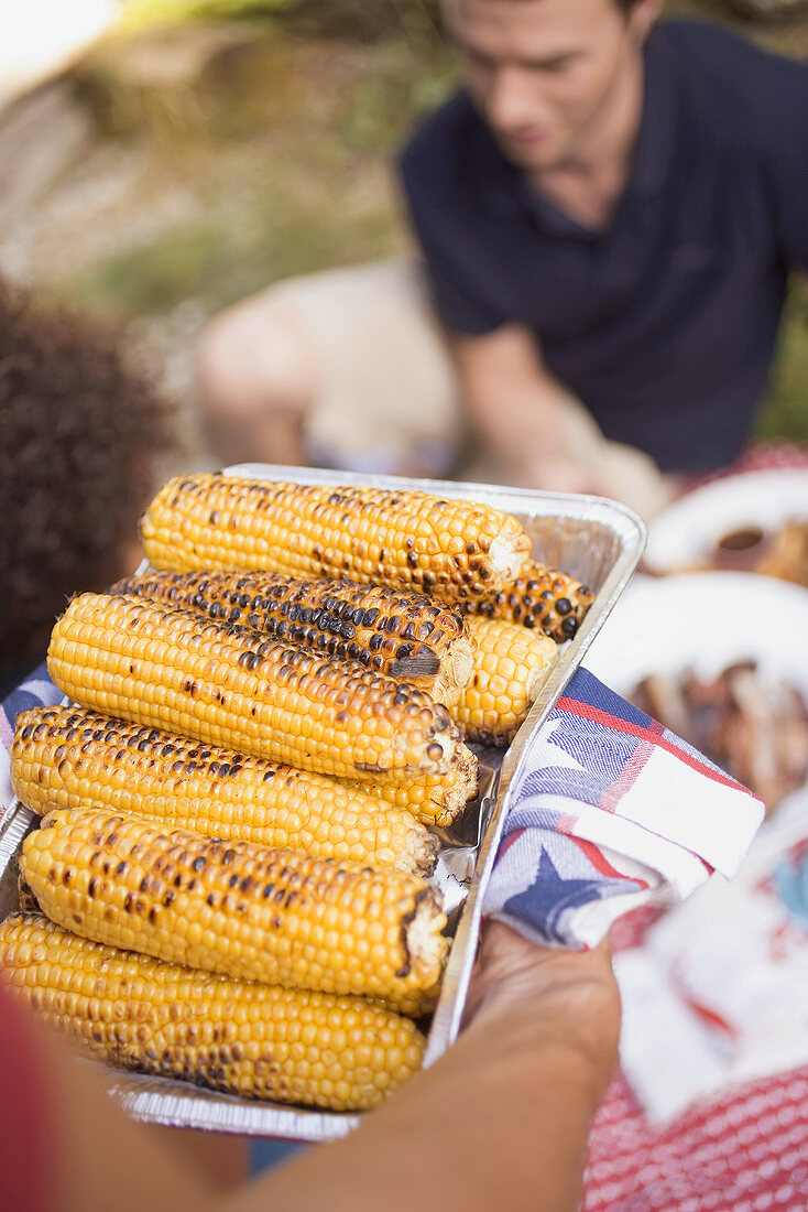 Man serving grilled corn on the cob on 4th of July (USA)