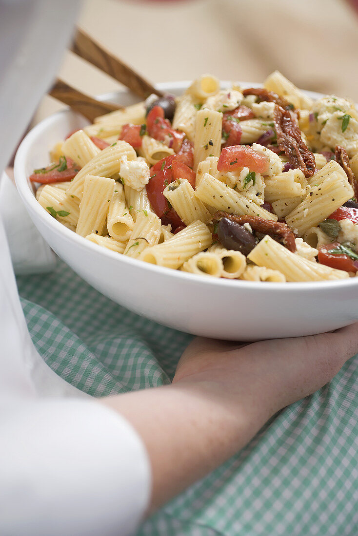 Frau hält Schüssel Nudelsalat mit Oliven und Tomaten