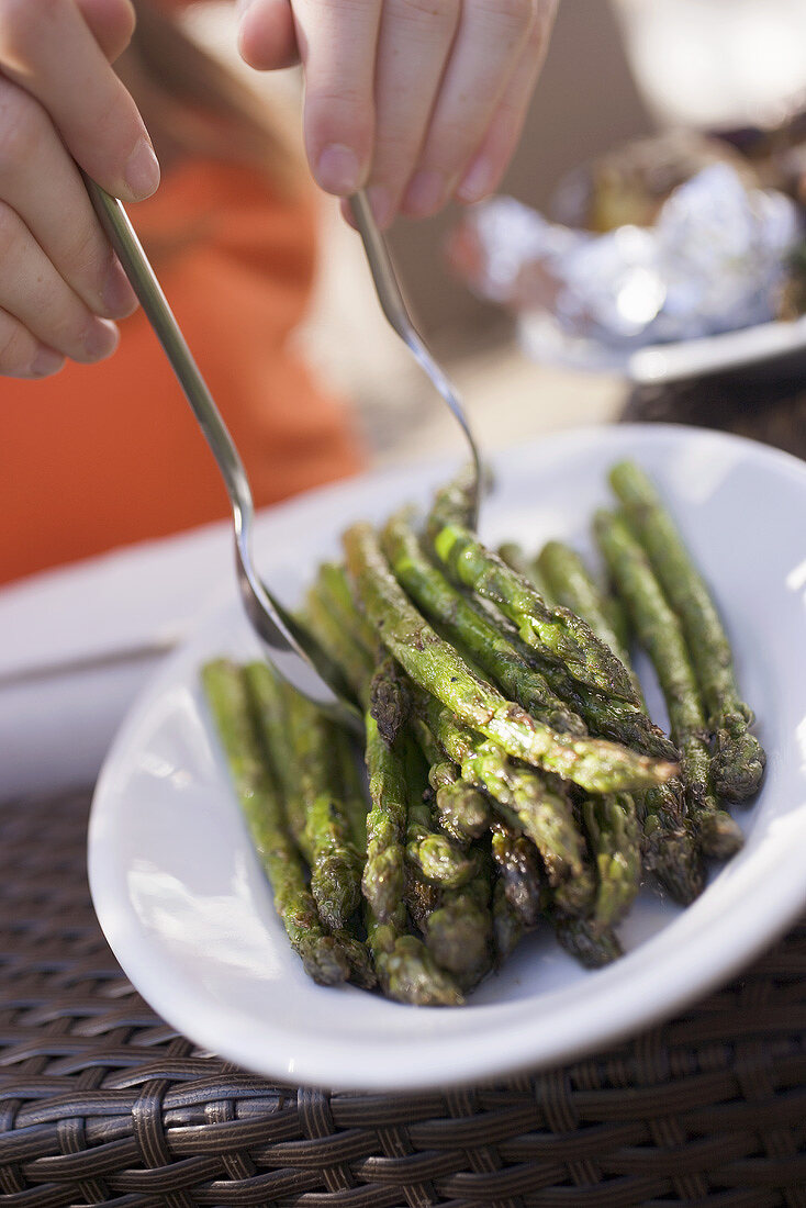 Person taking grilled asparagus from a plate
