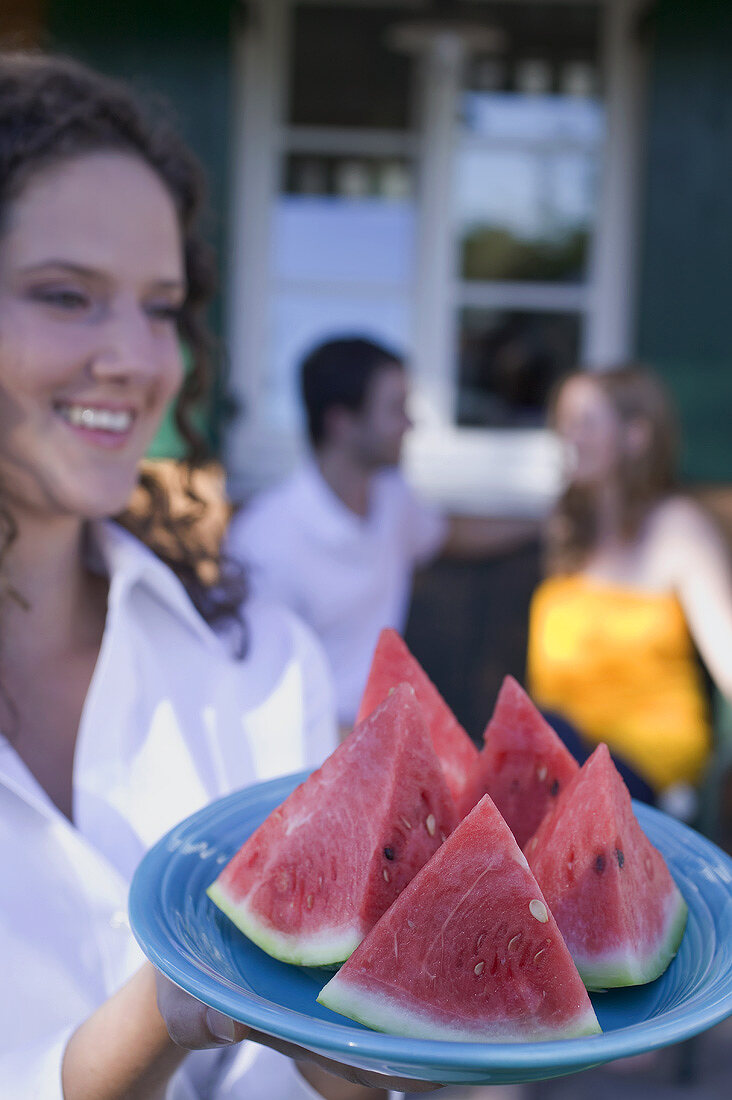 Woman serving watermelon wedges, couple in background