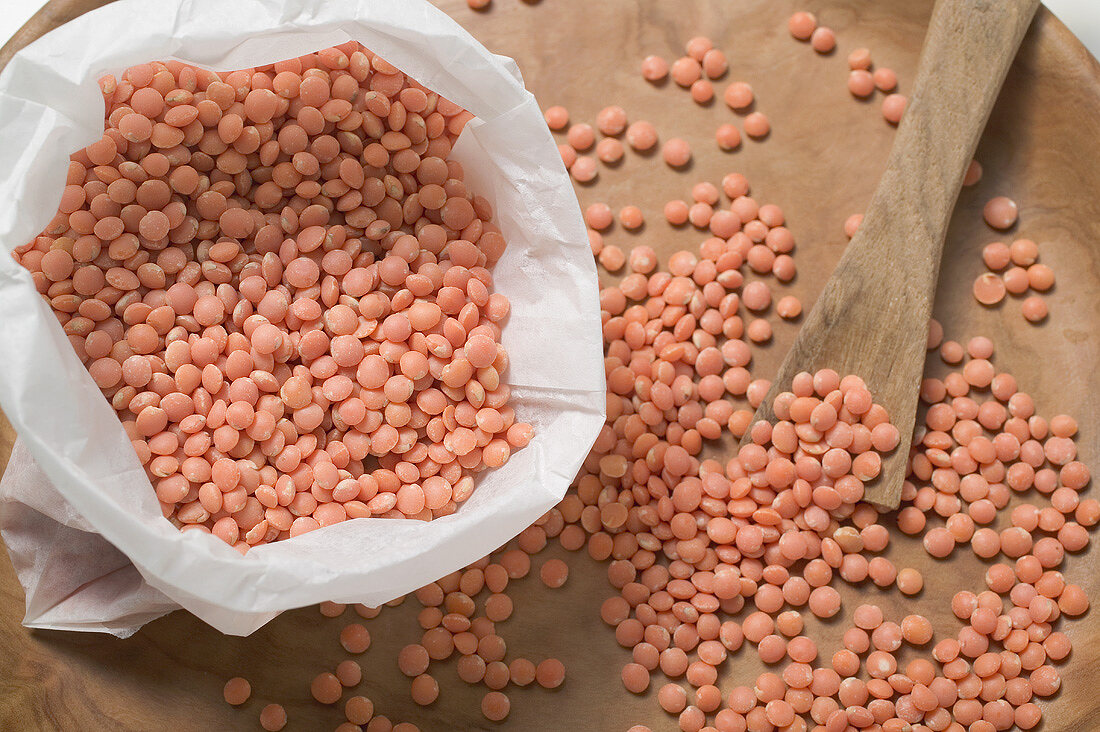 Red lentils on wooden plate and in bag (close-up)