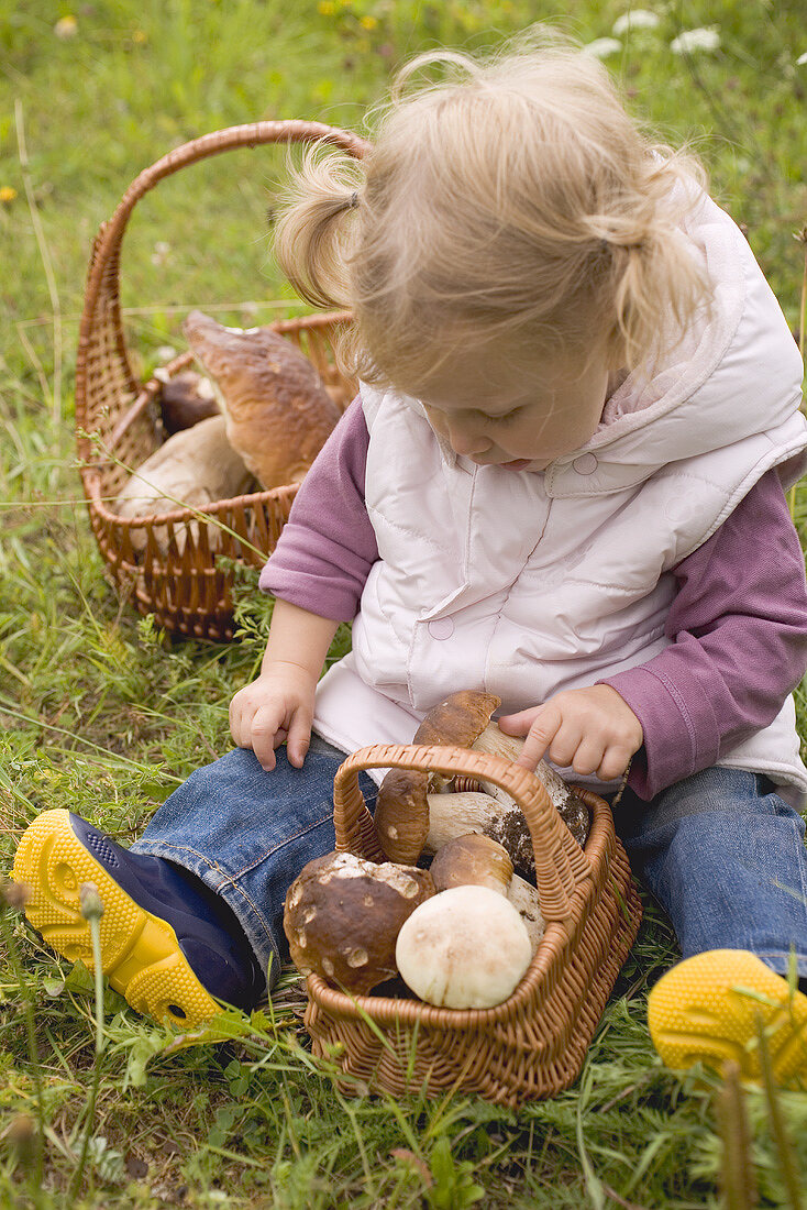 Kleines Mädchen mit Körben frischer Pilze auf Waldwiese