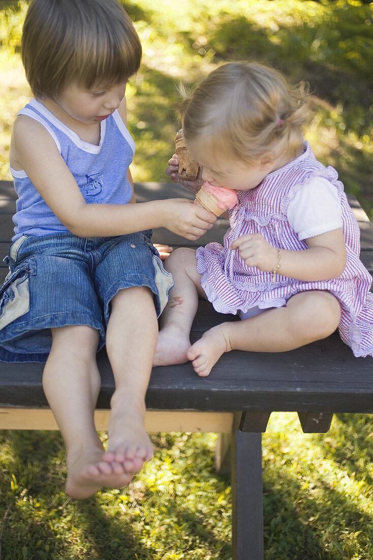 Zwei Kinder mit Eistüten auf Gartentisch