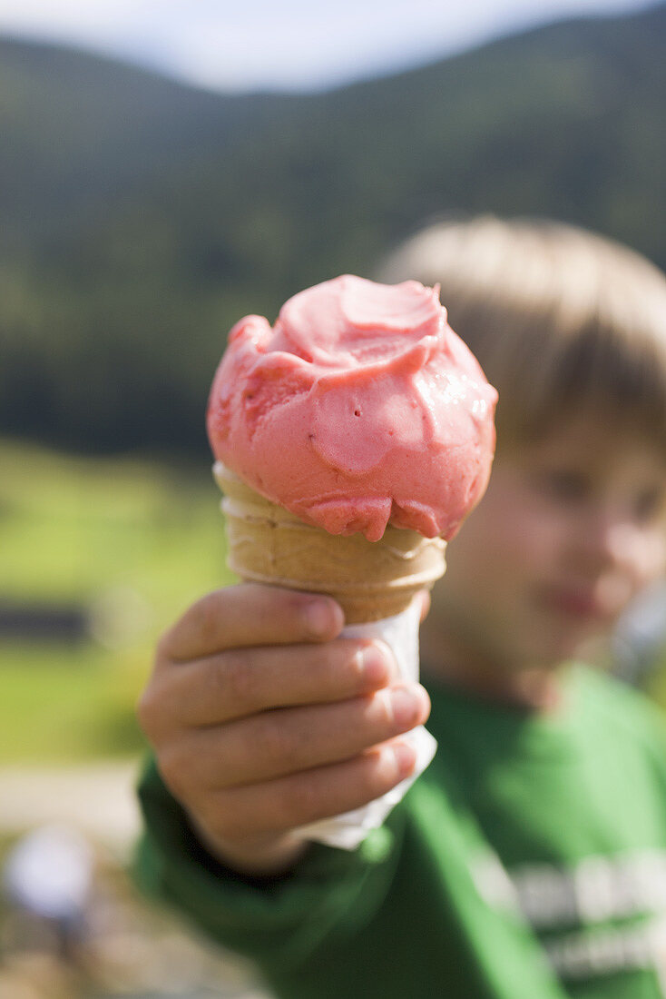 Small boy holding strawberry ice cream cone in outstretched hand