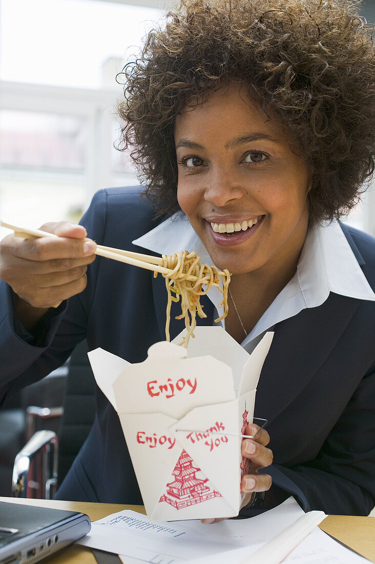 Frau im Büro isst asiatisches Nudelgericht