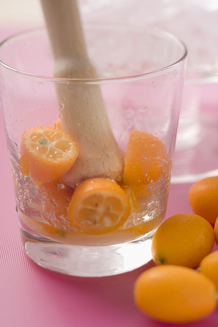 Making a cocktail with kumquats (crushing kumquats in a glass)