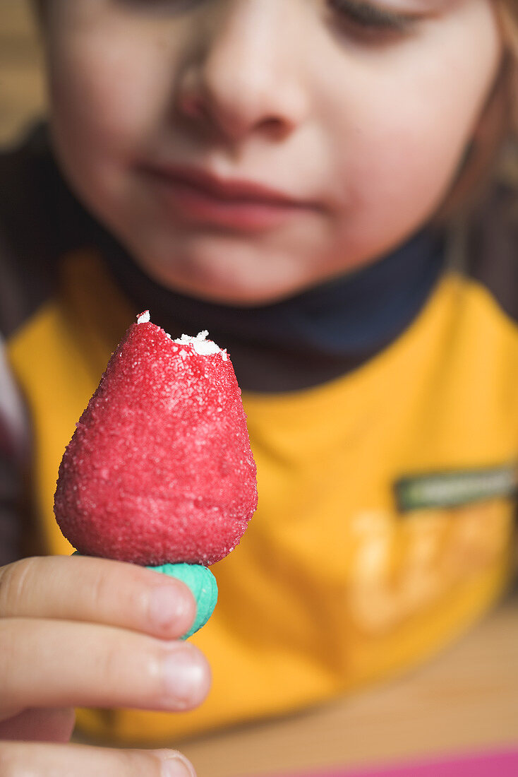 Child holding a marzipan strawberry with a bite taken