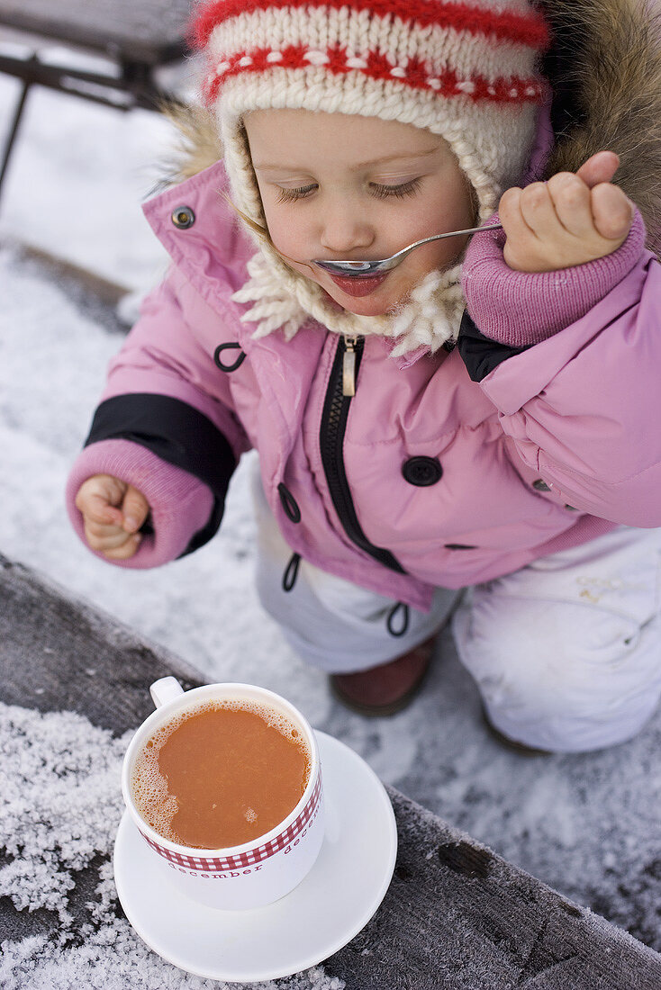 Small girl drinking cocoa from a spoon (out of doors)