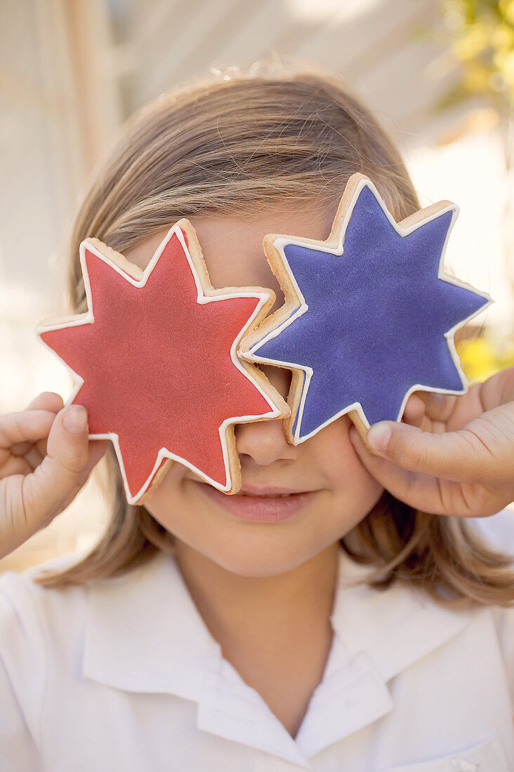 Small girl holding two star cookies in front of her eyes