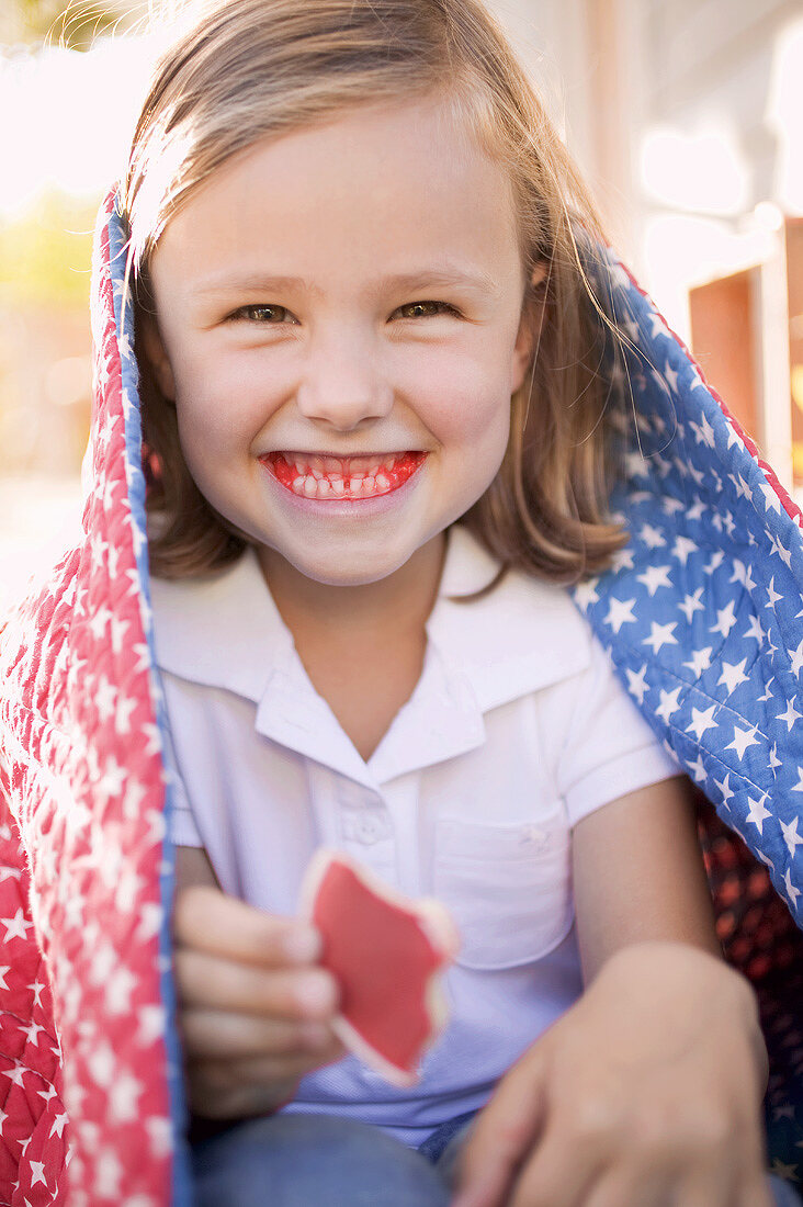 Kleines Mädchen mit angebissenem Keks und roten Zähnen (USA)