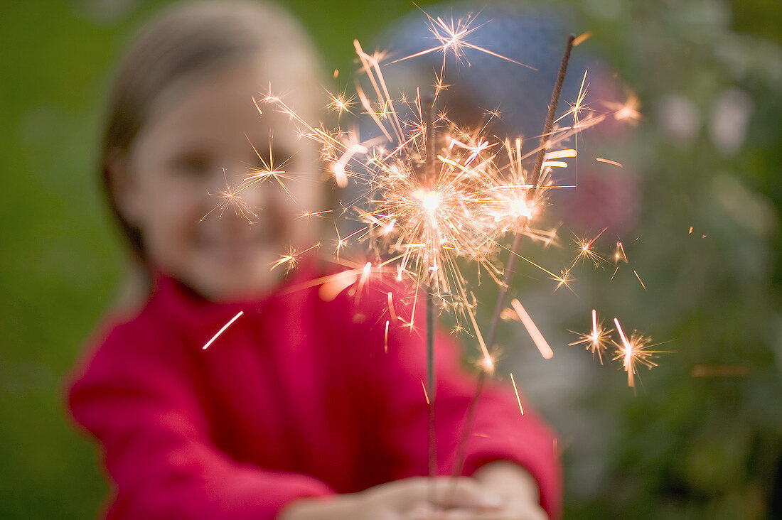 Small girl holding sparklers in garden