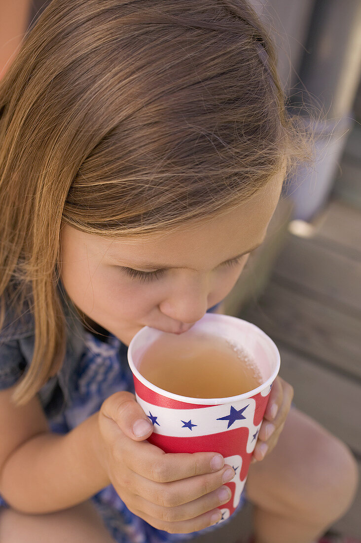 Kleines Mädchen trinkt Eistee aus Pappbecher