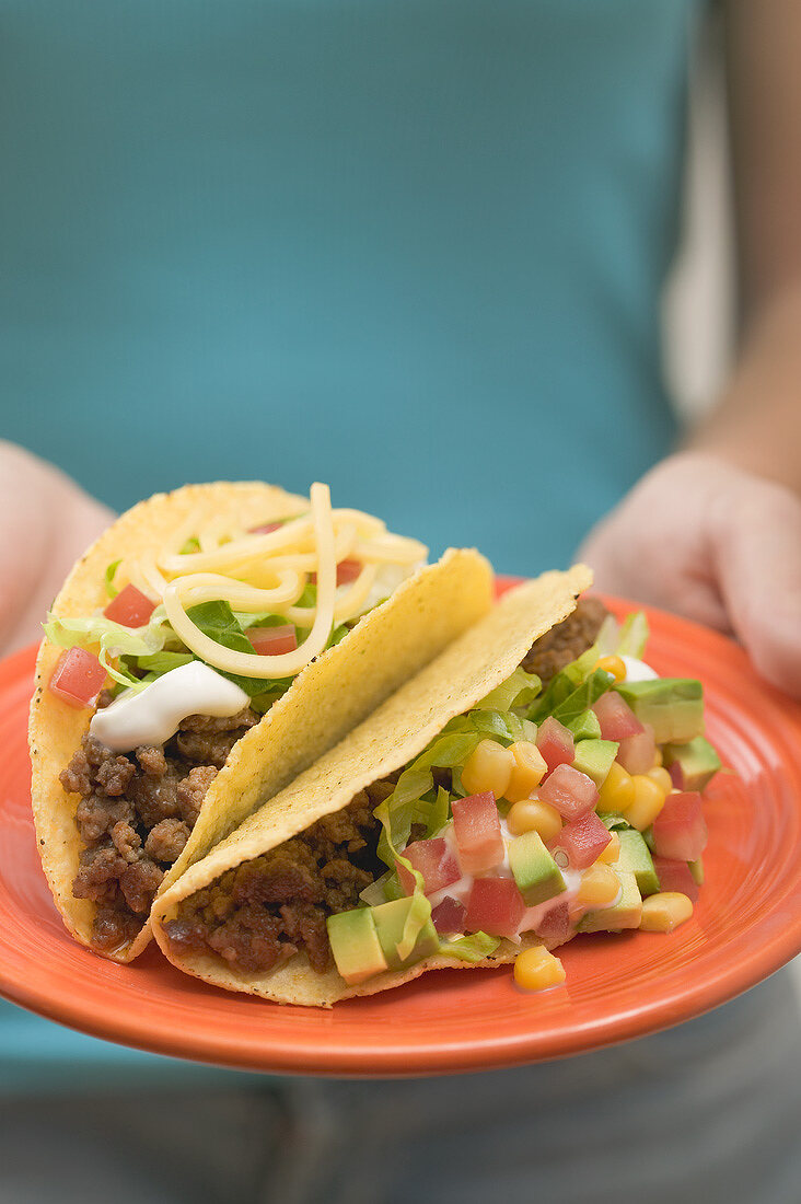 Frau hält Teller mit zwei Tacos