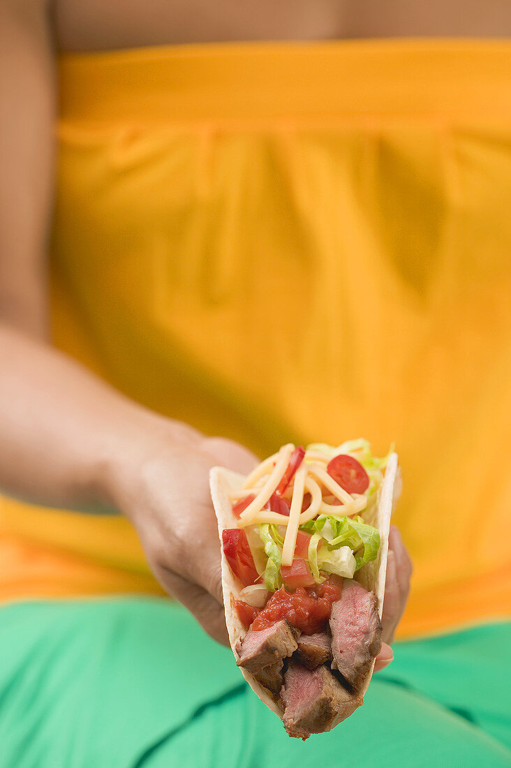 Woman holding a taco filled with beef, salad and cheese