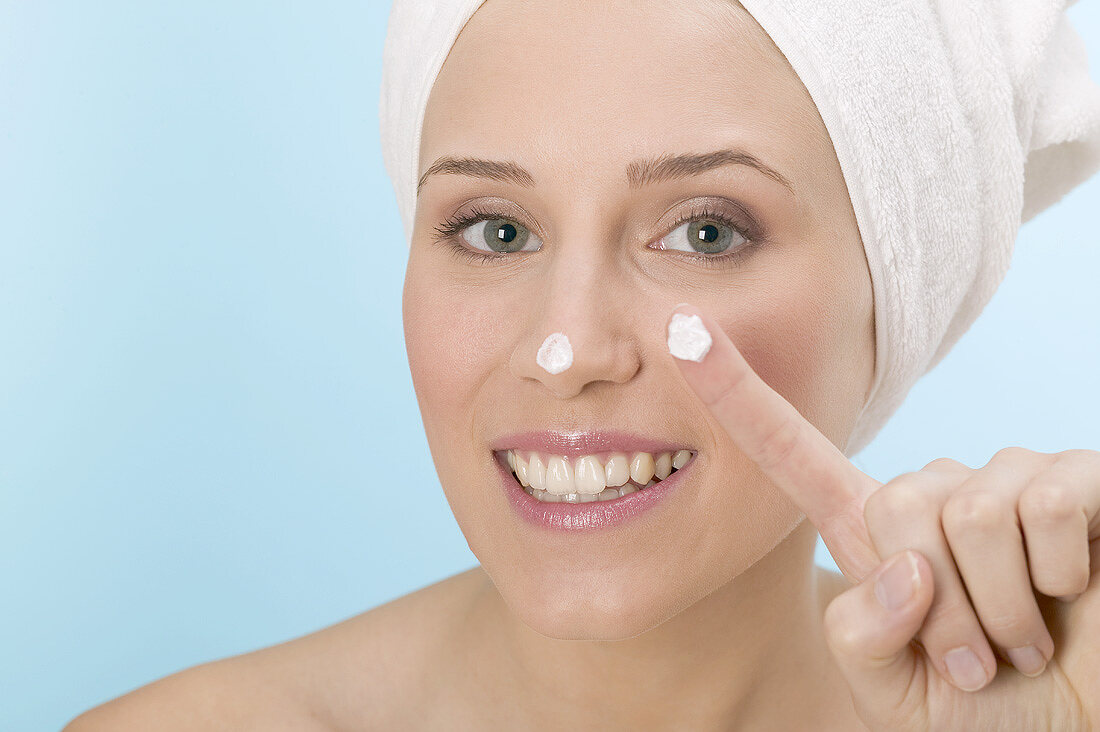Frau tupft Gesichtscreme auf Nase und Finger