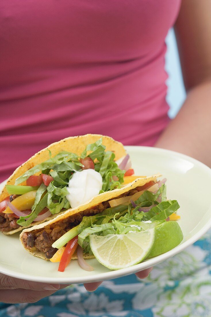 Frau hält Teller mit zwei Tacos