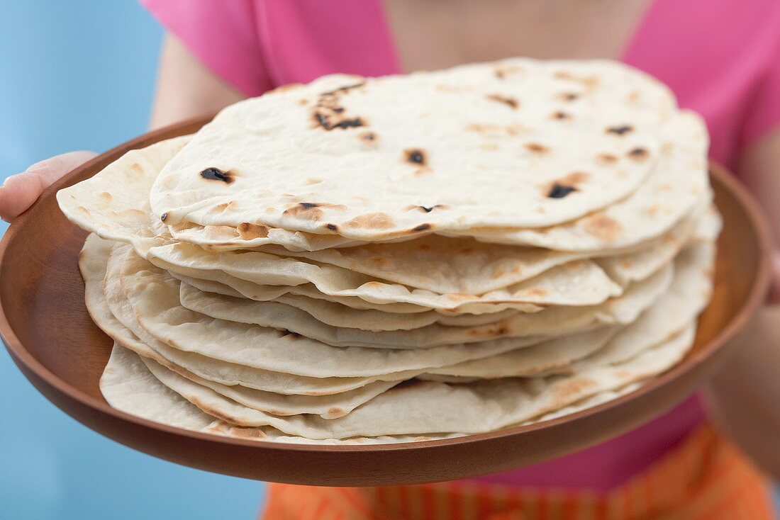 Woman holding freshly baked tortillas on tray