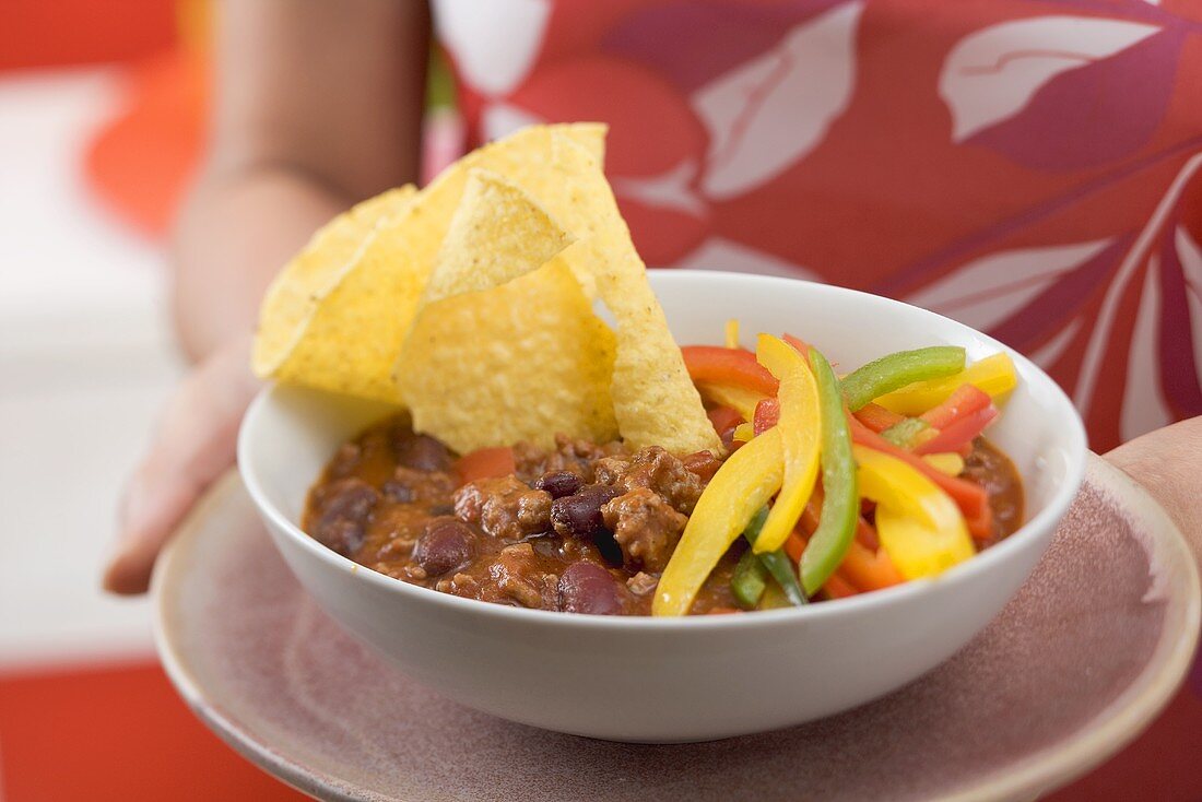 Frau serviert Chili con Carne mit Nachos und Paprika