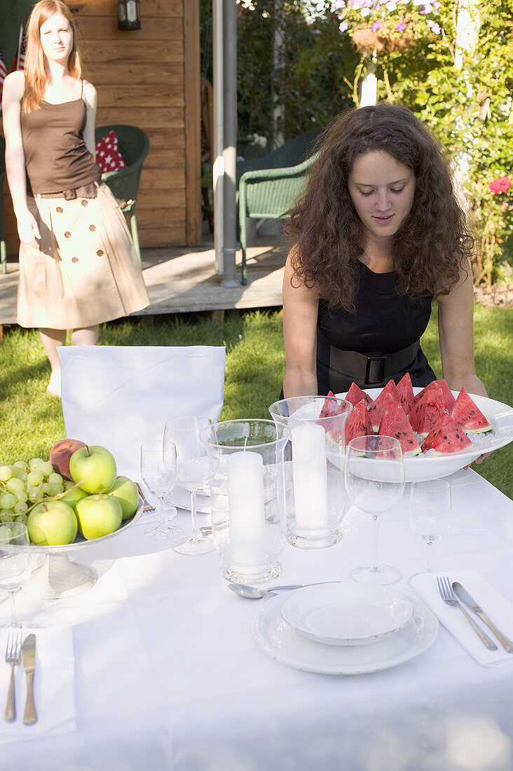 Frau trägt Melonenstücke zum gedeckten Tisch im Garten