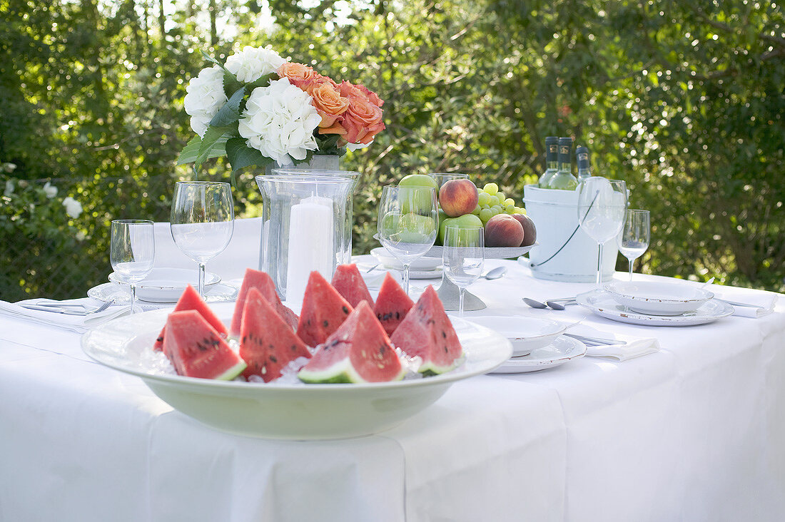 Gedeckter Tisch im Garten mit Wassermelone, Obstschale, Wein