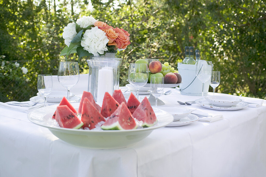 Watermelon, fruit and wine on table laid in garden