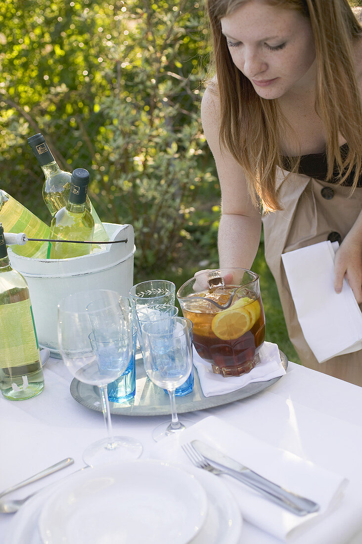 Woman putting a jug of iced tea on table laid in garden