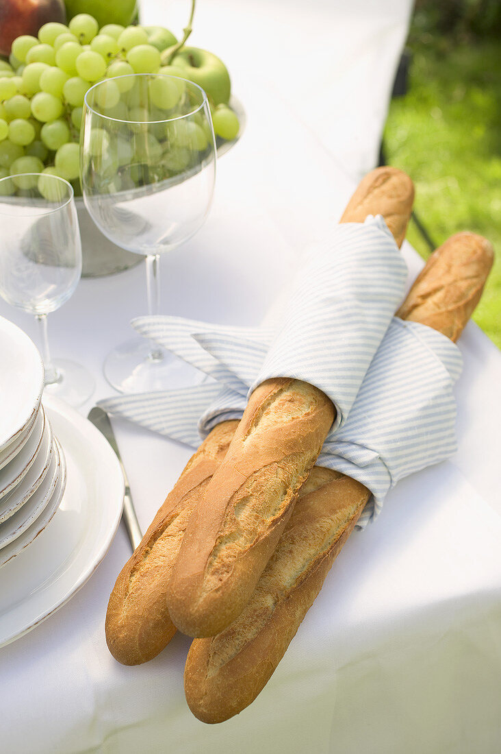 Baguettes, Weingläser und Obstschale auf Tisch im Freien