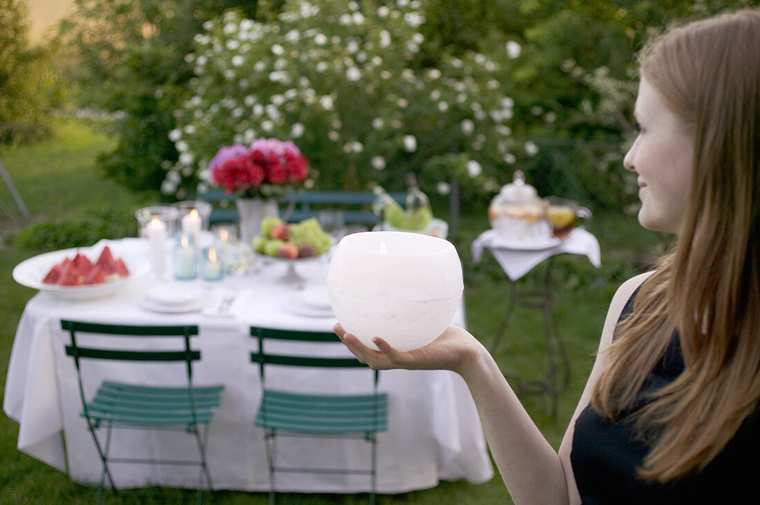 Woman holding windlight in front of table laid in garden