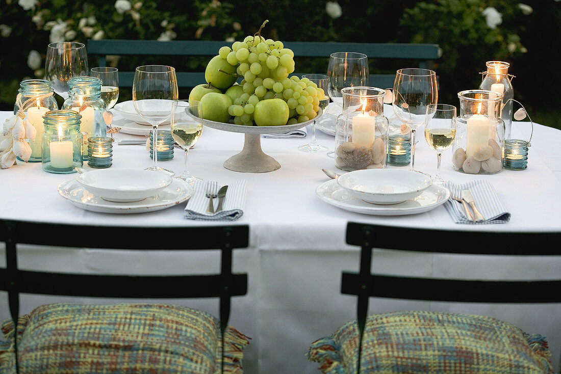 Bowl of fruit and windlights on table laid in garden