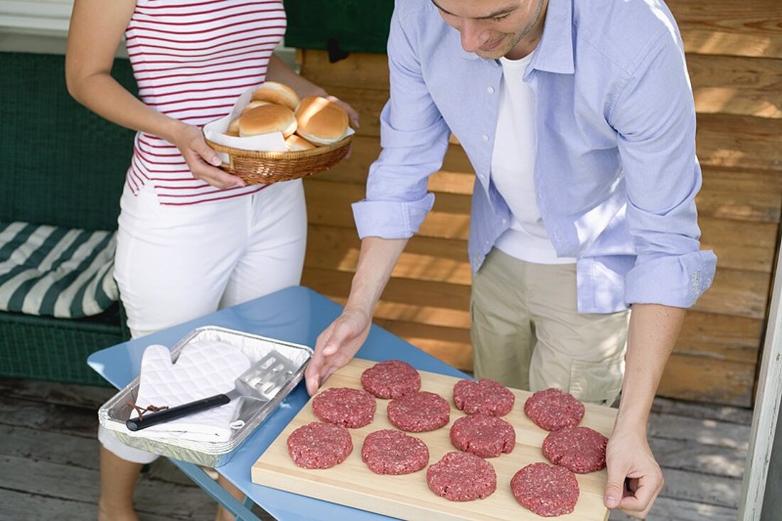 Man preparing burgers for grilling, woman bringing buns