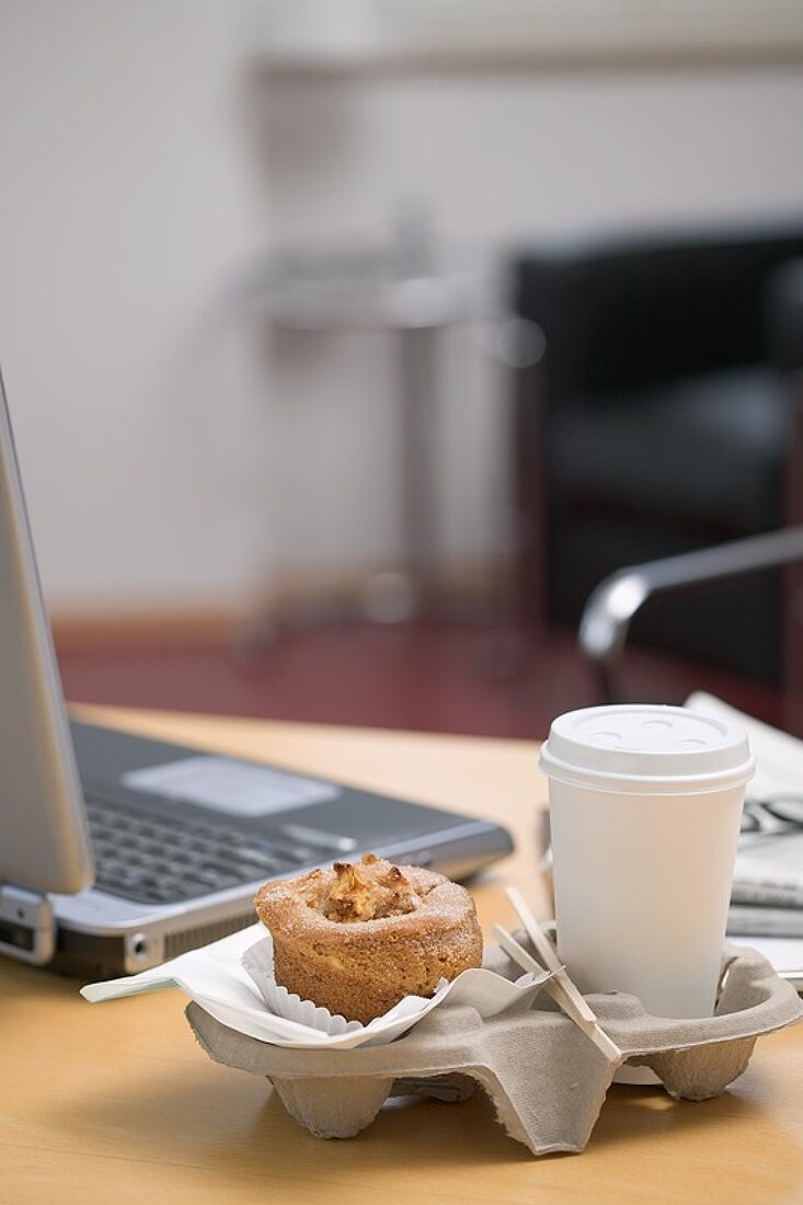 Muffin and cup of coffee beside laptop in office