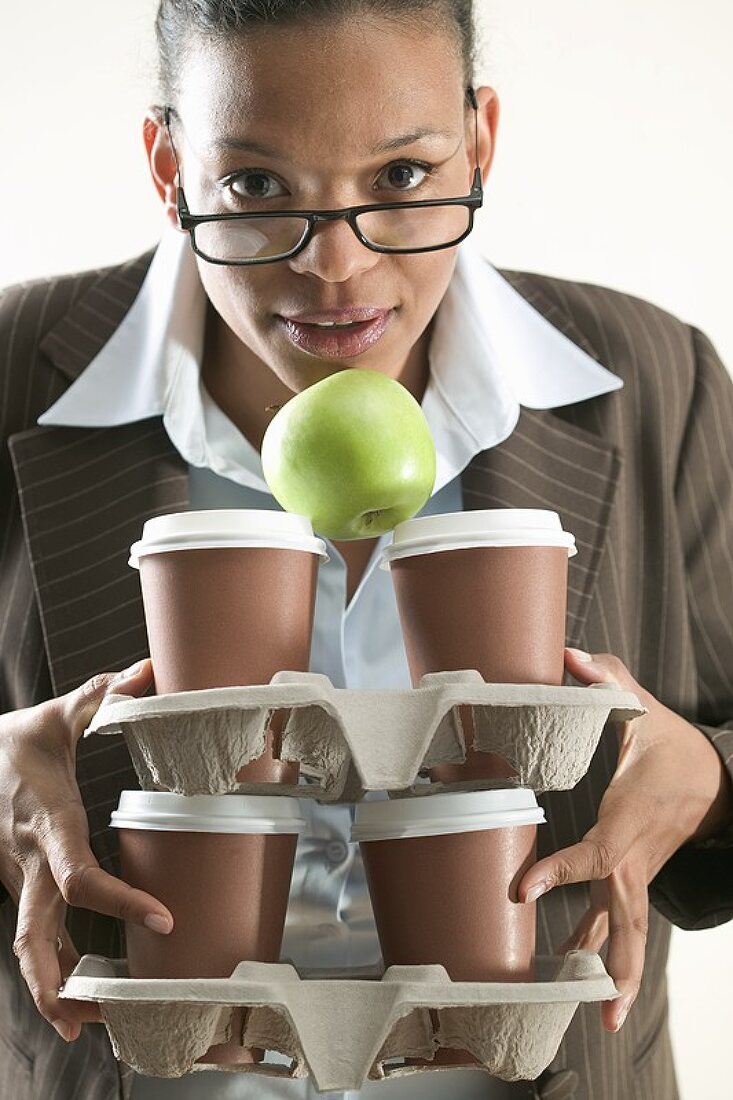 Geschäftsfrau hält vier Kaffeebecher und einen Apfel