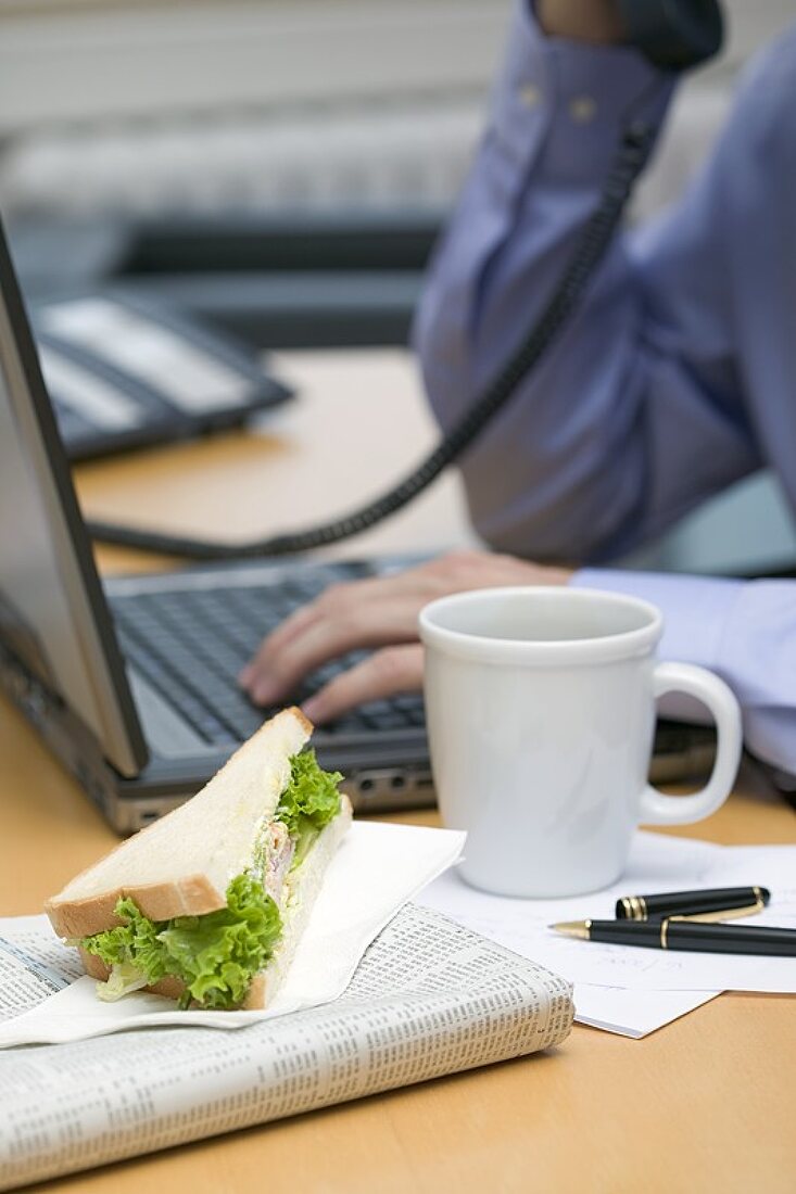 Businessman on phone, sandwich and coffee on desk