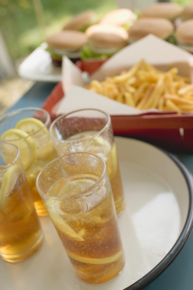 Iced tea, chips and hamburgers on table out of doors