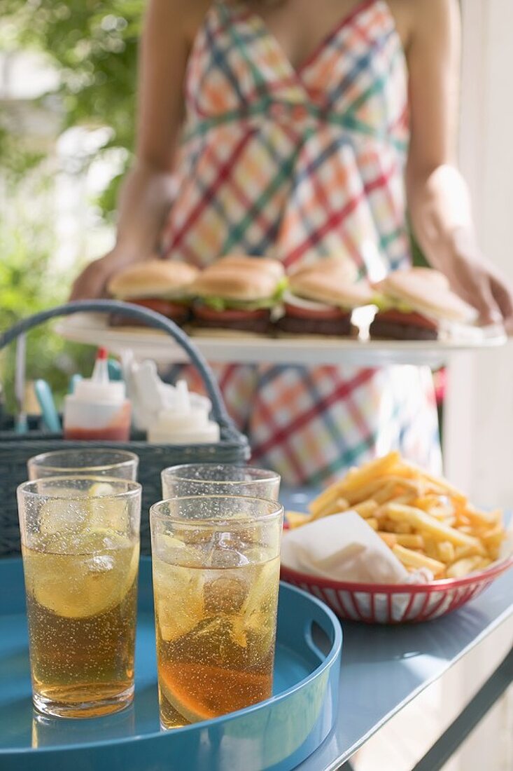 Eistee und Pommes frites auf Tisch, Frau serviert Hamburger