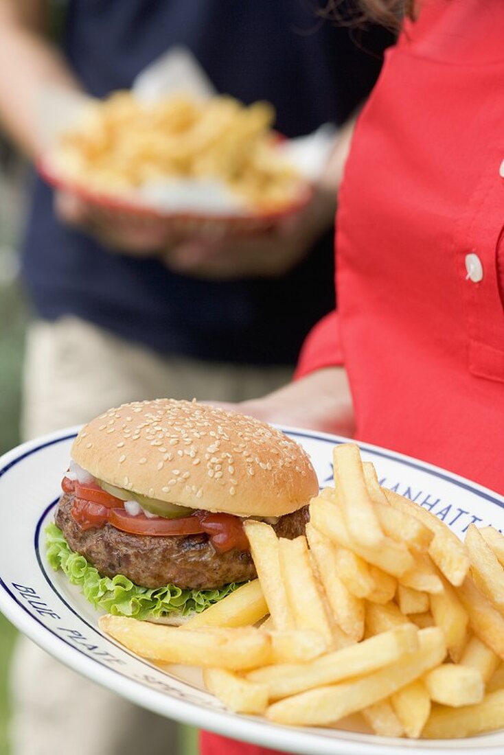 Frau hält Teller mit Hamburger und Pommes frites