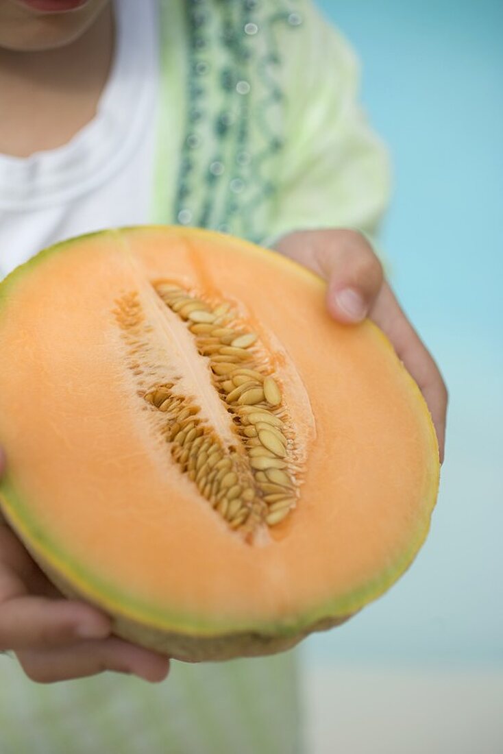 Kind hält halbe Cantaloupemelone